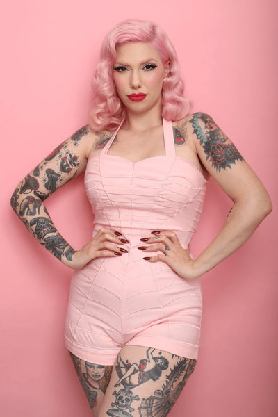 Shop Katakomb Charlotte Romper in baby pink for Valentine's Day. Spiderweb detailing and cute heart shaped pocket on the back of the shorts. Halter neck. Perfect for spring summer if you want a vintage pin up style 1940s 1950s look. Girly and curve flattering