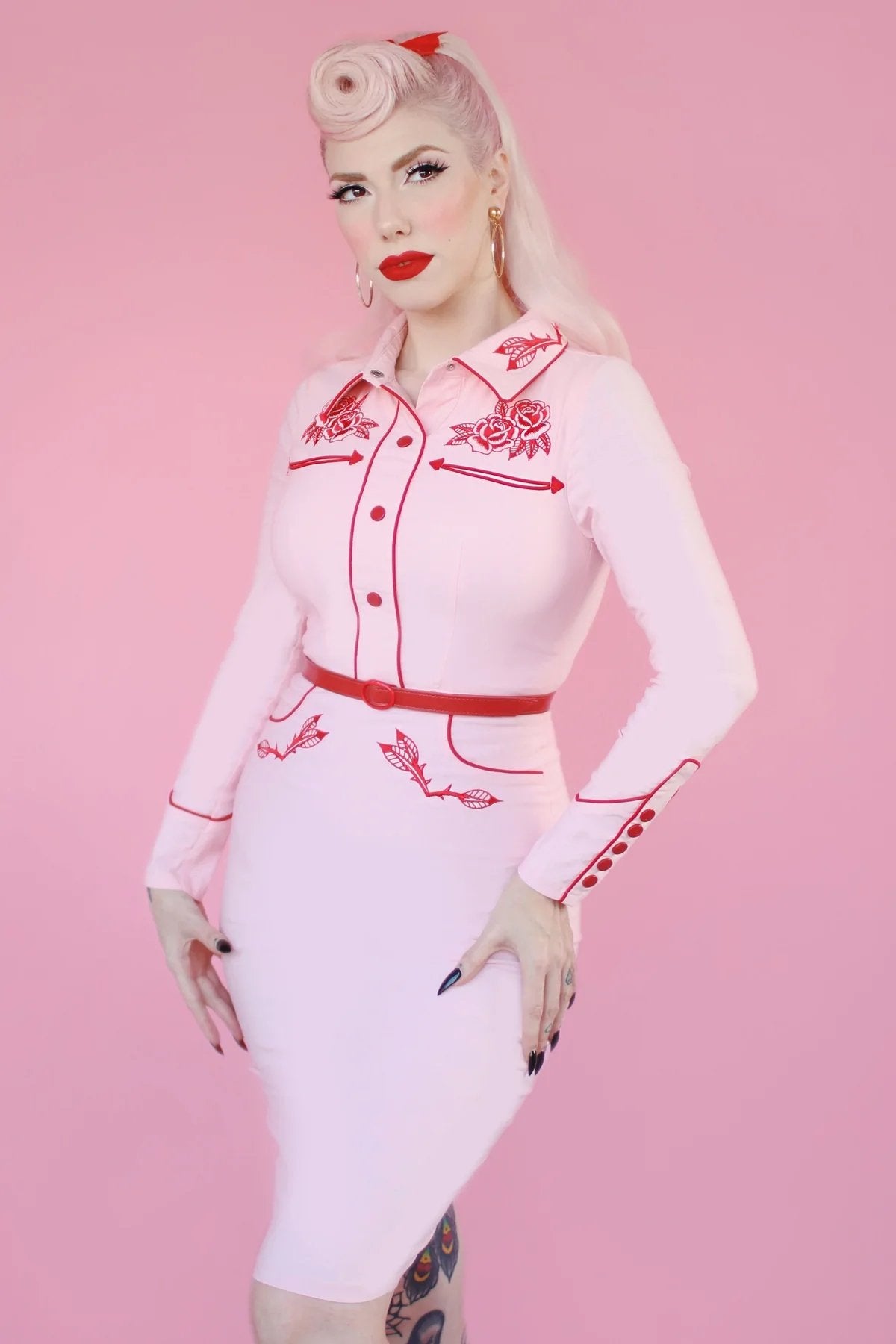Shop Katakomb June Carter western fitted wiggle dress in baby pink with red embroidery and detailing. Long sleeve with covered buttons and rose embellishments. Perfect for spring summer if you want a vintage pin up style 1940s 1950s look. Girly and curve flattering